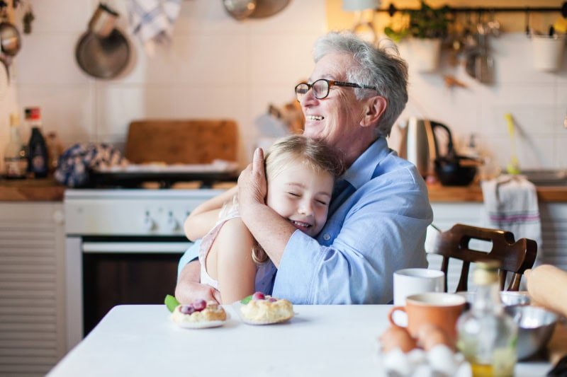 Why Do I Need a Humidifier in the Fall? Grandmother and young granddaughter laughing and hugging in an autumn decorated kitchen.